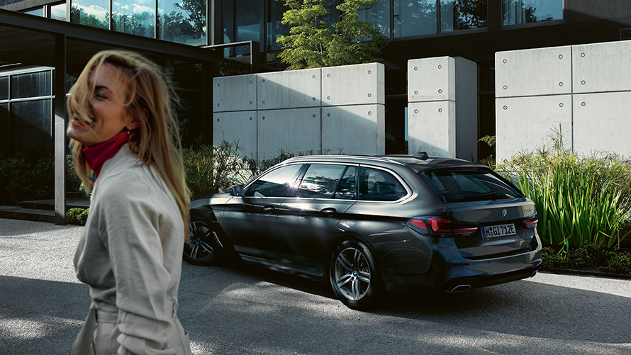 Women BMW 5er Touring G31 LCI Sophistograu Brilliant Effect metallic 7/8 Seitenansicht Frau vor parkendem BMW 5er Touring G31 Facelift 2020 in Sophistograu Brilliant Effect metallic 7/8 Seitenansicht