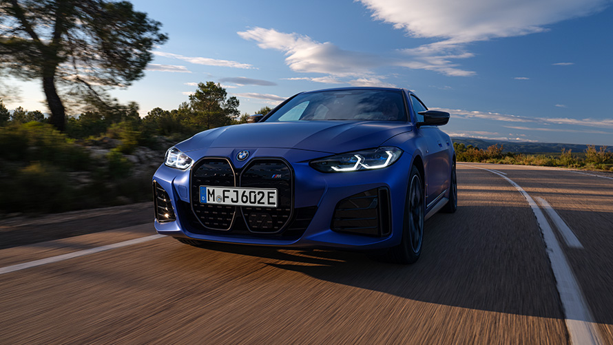 BMW i4 M50 G26 2021 BMW Individual Frozen Portimao Blue metallic front view driving BMW i4 M50 G26 2021 BMW Individual Frozen Portimao Blue metallic front view driving in front of fjord with hill in background