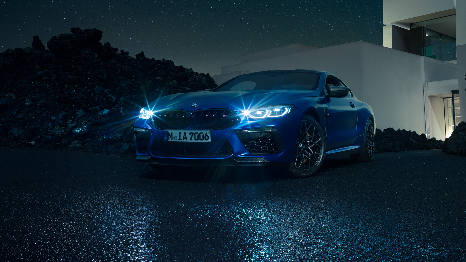 BMW M8 Competition Coupé, three-quarter front view. F92 BMW M8 Competition Coupé in Marina Bay Blue metallic with shining LED headlights, standing three-quarter front view in front of villa at night. F92