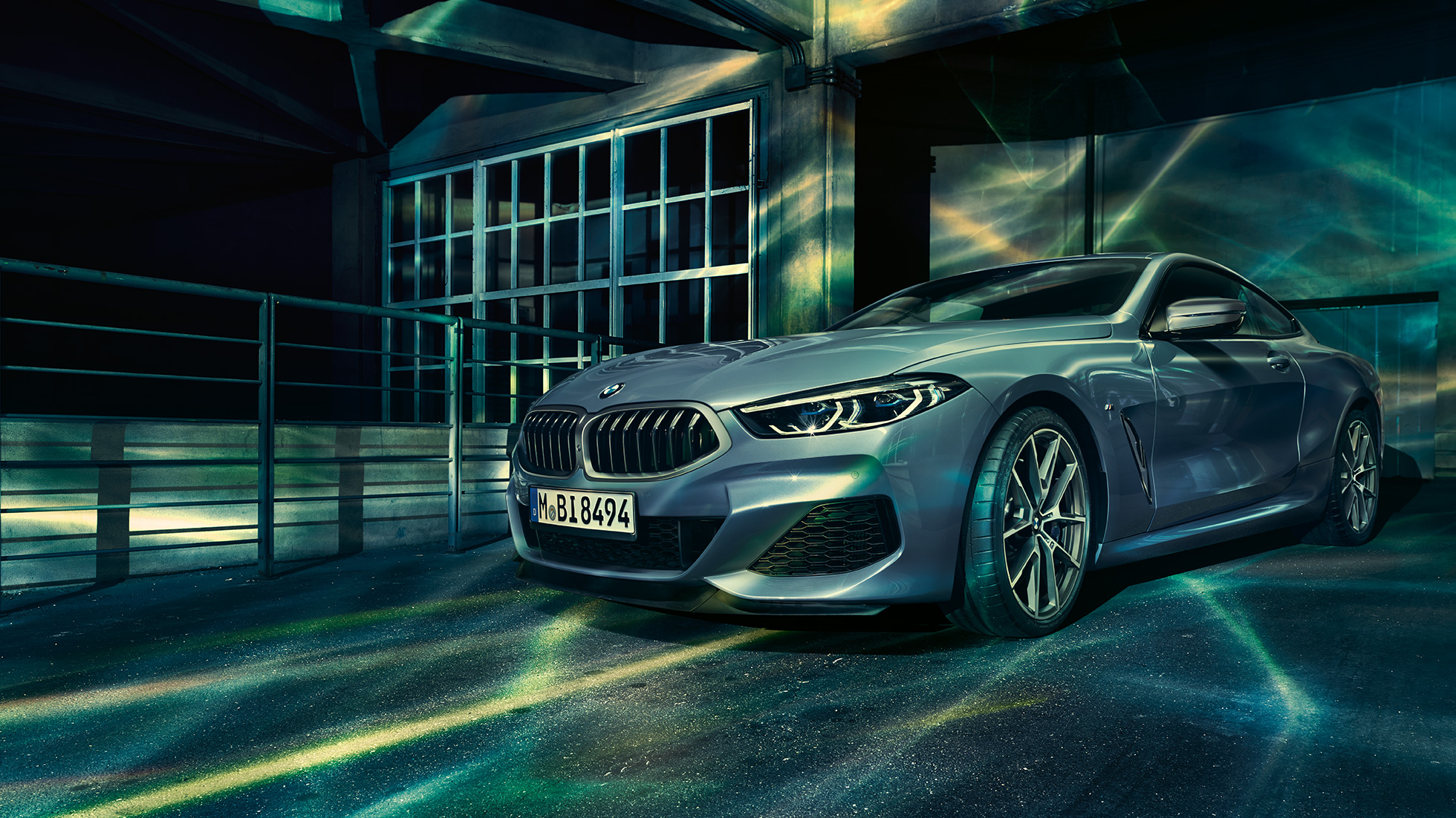 BMW M850i xDrive Coupé, three-quarter front view. BMW M850i xDrive Coupé in Barcelona Blue metallic, three-quarter front view standing in front of building.