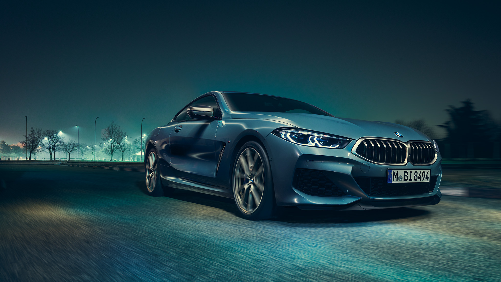 BMW M850i xDrive Coupé, three-quarter front view left. BMW M850i xDrive Coupé in Barcelona Blue metallic, three-quarter front view left, driving at night.