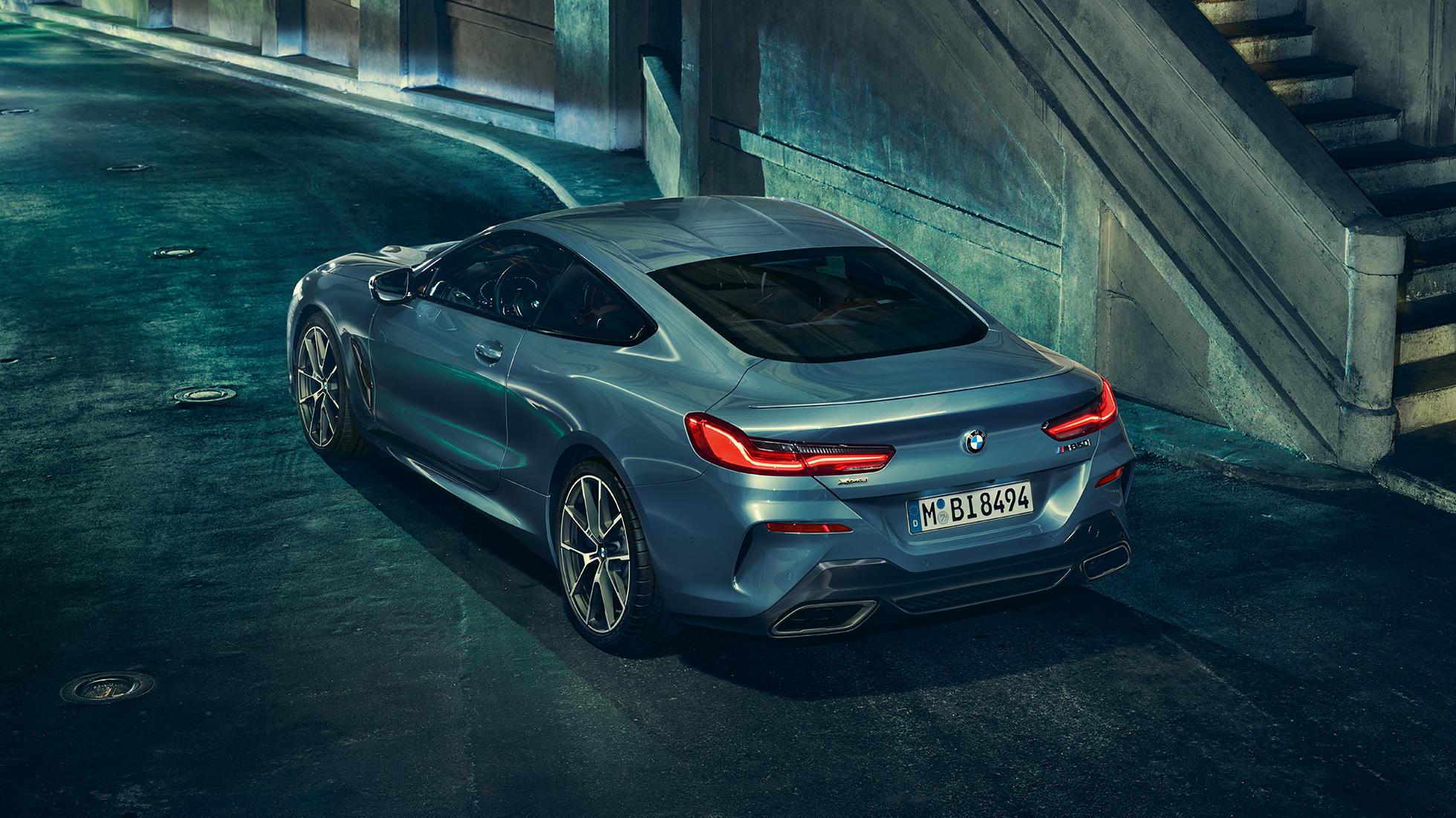 BMW M850i xDrive Coupé, three-quarter rear view left. BMW M850i xDrive Coupé in Barcelona Blue metallic, three-quarter rear view left, standing at night.