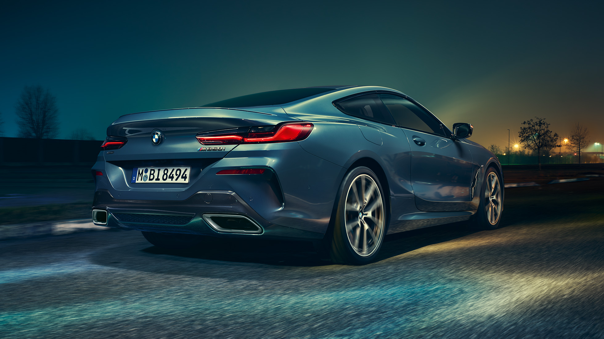 BMW M850i xDrive Coupé, rear view. BMW M850i xDrive Coupé in Barcelona Blue metallic, rear view, driving at night.