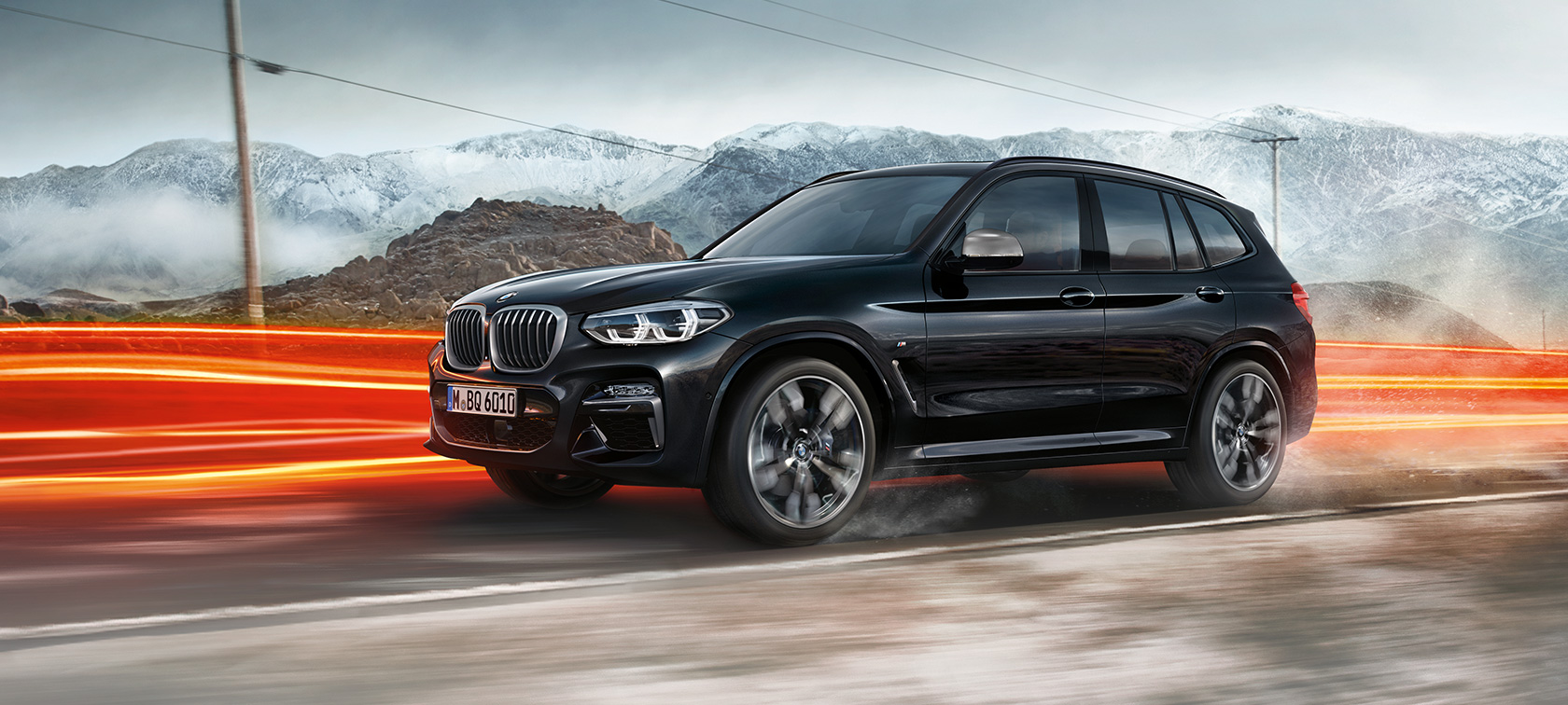 BMW X3 M40i and BMW X3 M40d, side view. BMW X3 M40i and BMW X3 M40d in Black Sapphire metallic, driving, exterior, side view in front of mountain scenery with light strips.