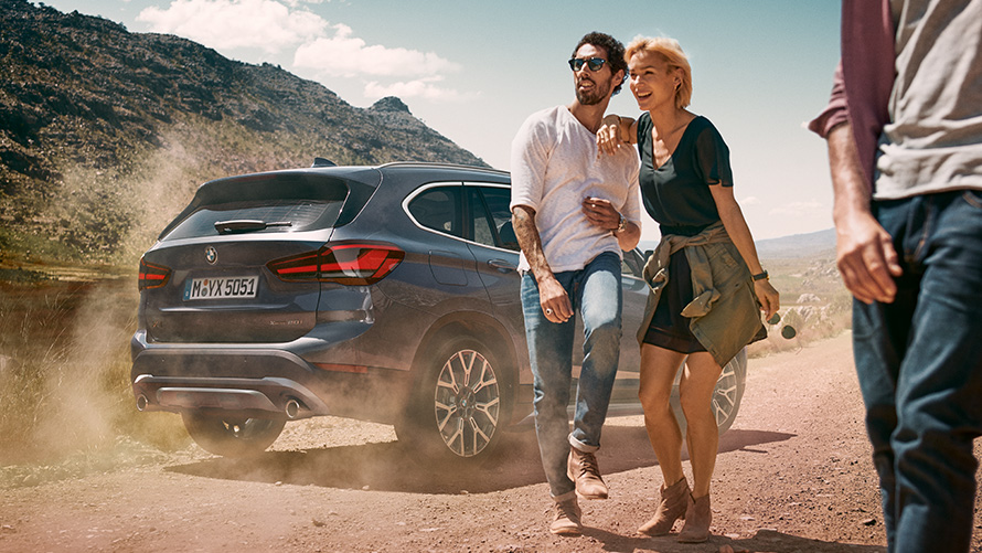 BMW X1 F48 LCI Storm Bay Three-quarter rear view BMW X1 F48 LCI Storm Bay Three-quarter rear view standing in landscape with people in front of it