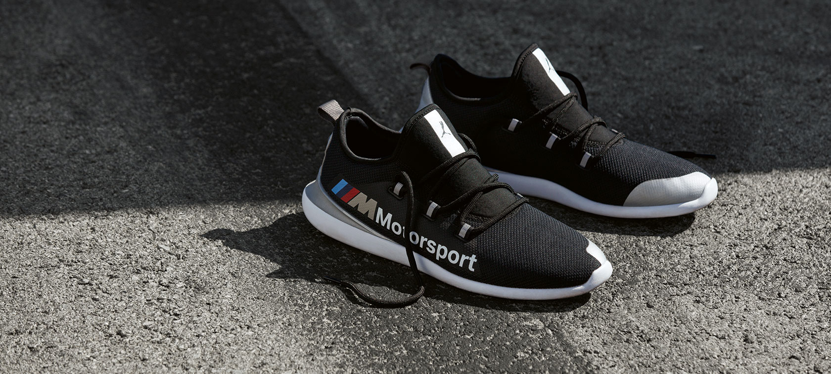 BMW M Motorsport PUMA EVO CAT Shoes. A pair of BMW M Motorsport PUMA EVO CAT Shoes from the BMW M Motorsport Collection is shown standing on a tarmac surface.