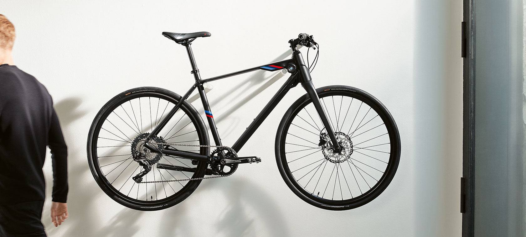 BMW M Bike Matt Black. The picture shows a BMW M Bike Matt Black with BMW M Motorsport branding stripes hanging on a wall bracket.