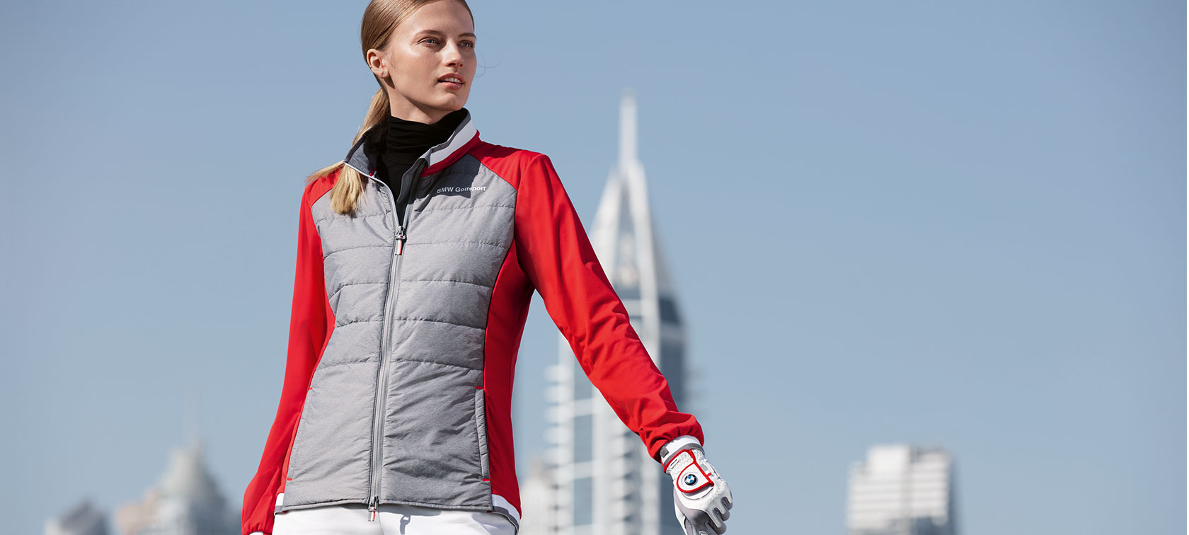 BMW Golfsport Ladies Jacket. The young woman in the picture presents premium articles from the BMW Golfsport Collection against the backdrop of a big city skyline.