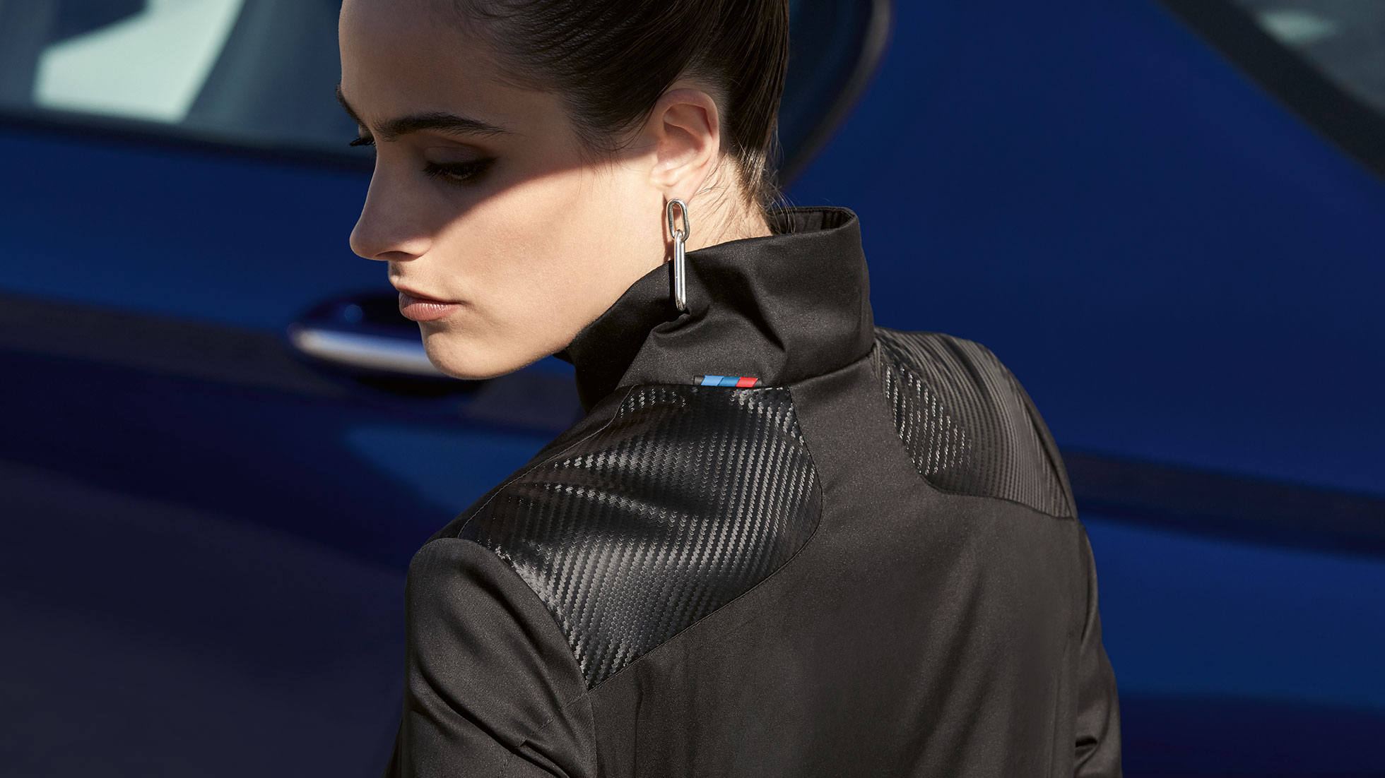 BMW M Jacket, ladies. A woman is shown wearing a BMW M Jacket, ladies from the BMW M Collection. Detail of the materials mix.