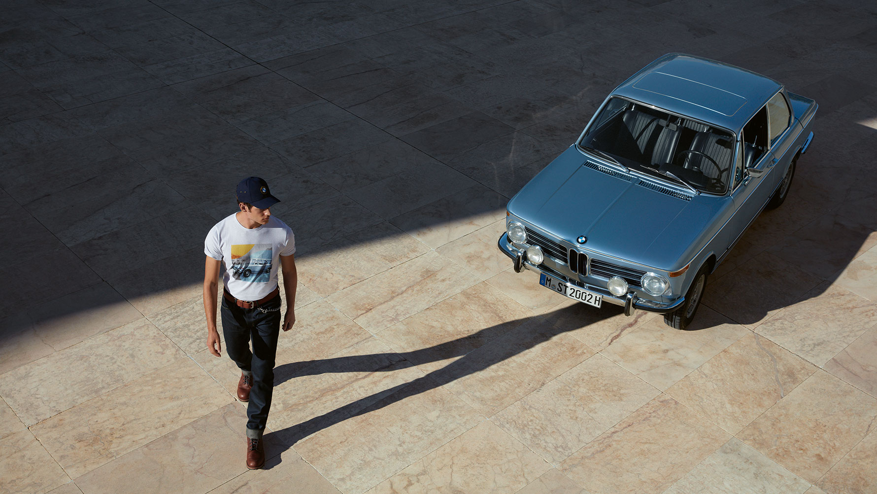 A man wearing a BMW Classic Men's T-shirt is shown admiring a classic BMW. A man wearing a BMW Classic Men's T-shirt is shown admiring a classic BMW.