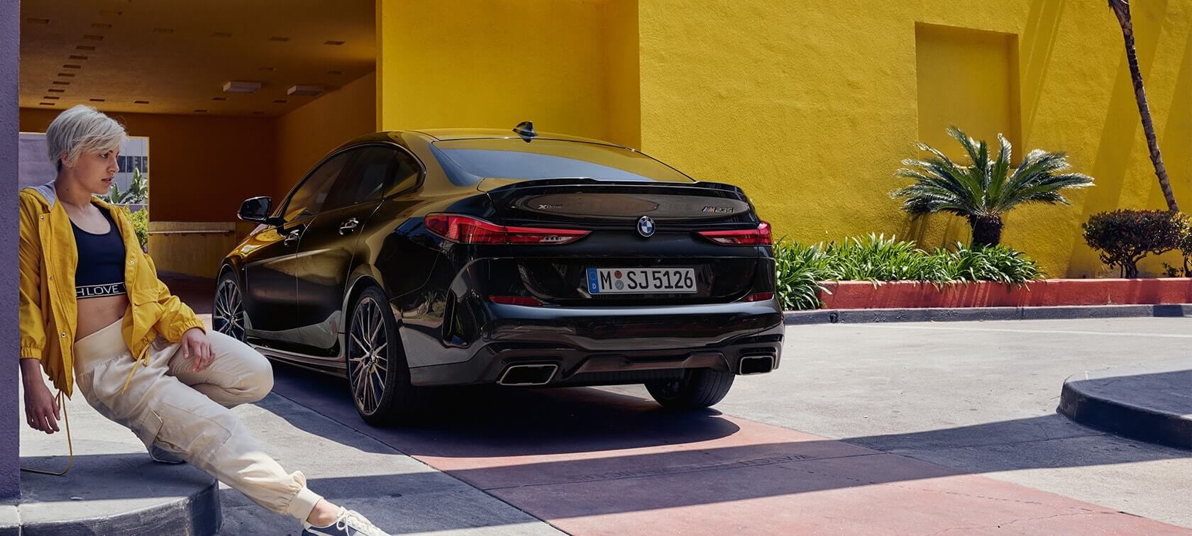 BMW M235i xDrive Gran Coupé three-quarter rear view BMW M235i xDrive Gran Coupé Black Sapphire metallic F44 three-quarter rear view with woman in the front
