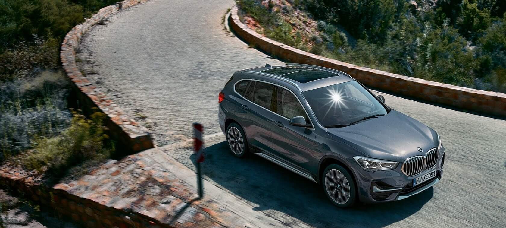 BMW X1, three-quarter front view. F48 BMW X1, three-quarter front view driving in front of mountain scenery. F48
